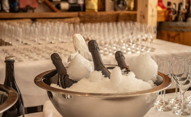 Eisgekühlte Flaschen in einem Behälter mit Gläsern im Hintergrund.