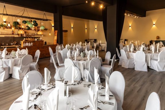 Eleganter Speisesaal mit runden Tischen, weißen Stuhlhussen und stimmungsvollem Licht.