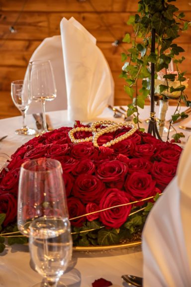 Ein Tischgedeck mit roten Rosen und eleganten Gläsern für eine festliche Veranstaltung.