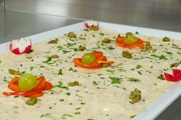 Cremige, dekorierte Speise mit Radieschen, Trauben und Kräutern auf einer weißen Platte.