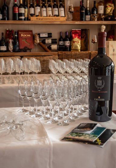 Rotweinflasche neben Gläsern auf einem Tisch, mit Weinkarte im Vordergrund.